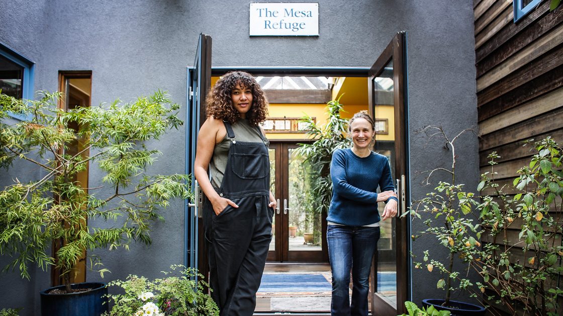 Two people stand in the open doorway beneath “The Mesa Refuge” sign.